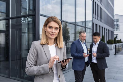 Portrait of successful senior woman businessman and specialist, program manager with tablet computer outside office building smiling and looking at camera, professional programmer team leader.