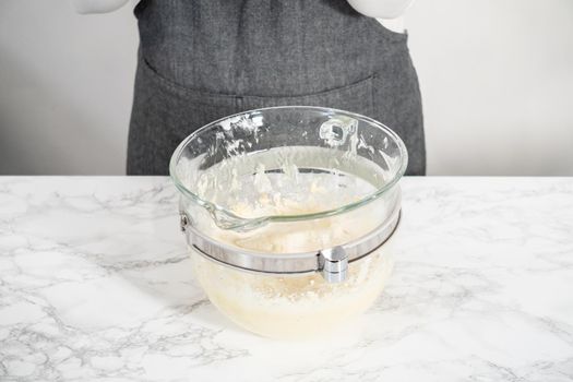 Mixing ingredients in a large glass mixing bowl of kitchen mixer to make eggnog buttercream frosting.