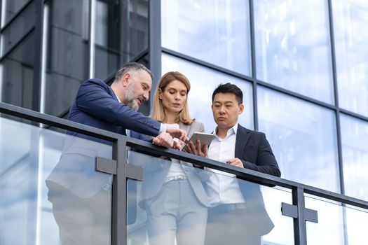 Specialist IT team leaders, group of business people outside office building, discussing and talking, testing new app on tablet, professional colleagues in business clothes,