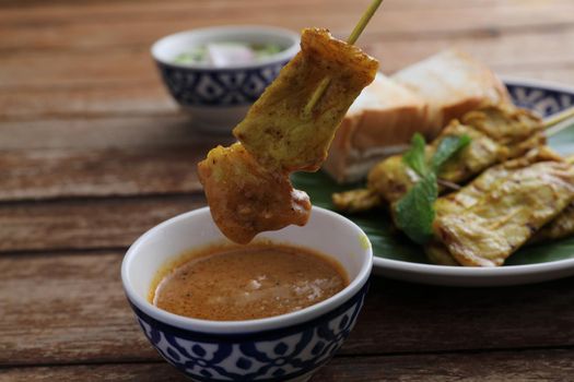 Local Thai food pork satay with oeanut dipping sauce isolated in wood background