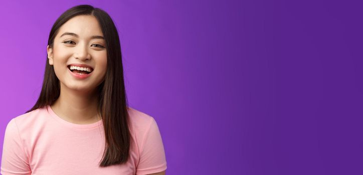 Close-up lively carefree cheerful asian girl laughing, having fun, smiling amused enjoy friendly relaxing conversation, stand purple backgrond joyful, look camera upbeat. Copy space