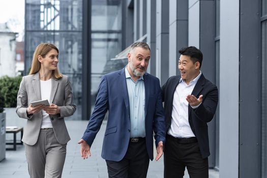 A diverse team of IT specialists, senior and experienced engineers managers team leaders, a group of three workers happily strolling outside an office building, colleagues in business suits.