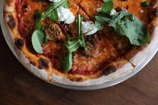 Italian Sausage and rocket salad pizza on wood background