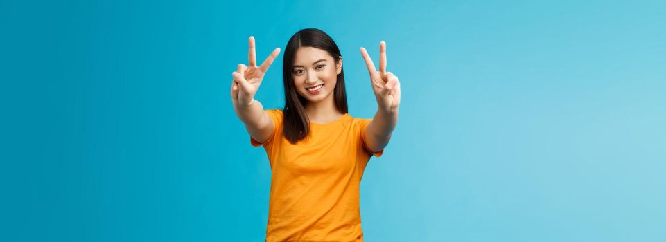 Positive upbeat cute asian girl believe win, aim success extend hands show victory, peace sign smiling broadly, have happy enthusiastic mood, spend carefree vacation travel abroad value pacifism.