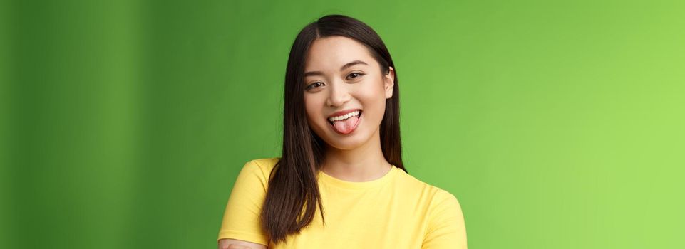 Close-up silly cute flirty asian girl fool around childish, playfully communicate boyfriend, show tongue smiling broadly, cross hands chest casually, enjoy summer holidays, green background.