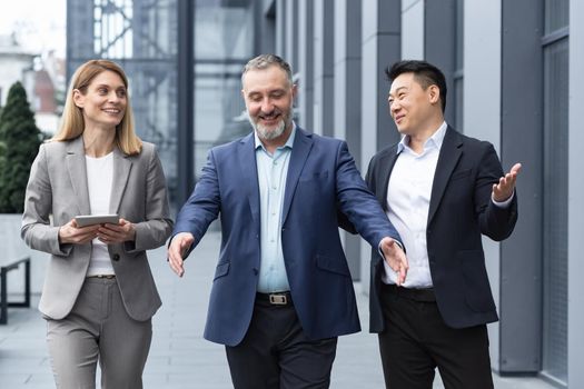 A diverse team of IT specialists, senior and experienced engineers managers team leaders, a group of three workers happily strolling outside an office building, colleagues in business suits.