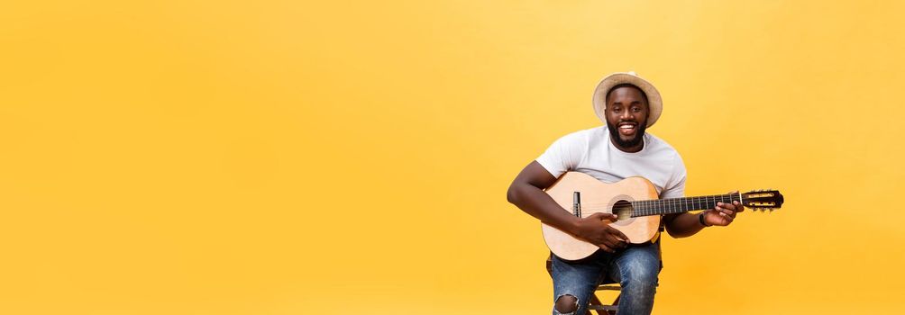 Muscular black man playing guitar, wearing jeans and white tank-top. Isolate over yellow background