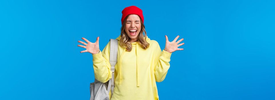 Carefree happy girl relieved finally classes are over and summer vacation starting, screaming from joy and positive emotions with closed eyes shaking hands happily, carry backpack.