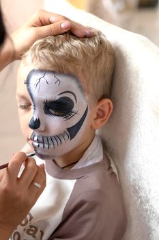 A makeup specialist girl makes a festive creepy makeup for a boy for the Halloween holiday in the studio. Happy Halloween concept. High quality photo