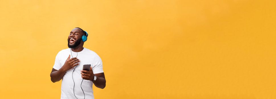 African American man with headphones listen and dance with music. Isolated on yellow background.