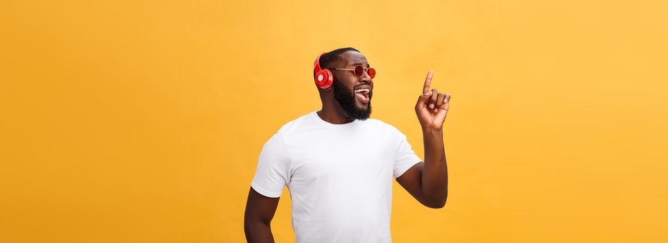 Handsome young African American man listening and smiling with music on his mobile device. Isolated over yellow background