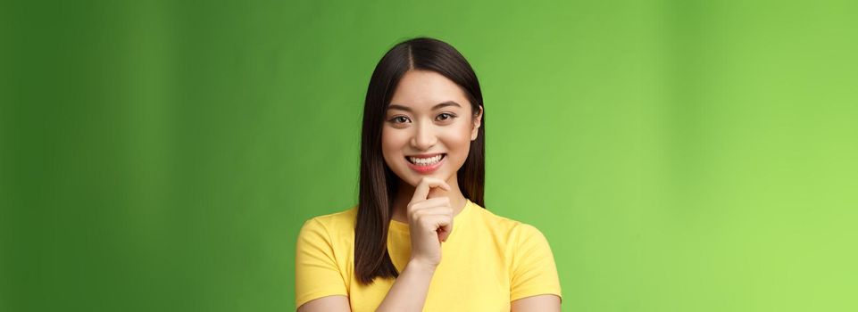 Smart assertive creative asian female student make interesting research assumption, smiling intrigued touch chin thoughtful, have good plan idea, thinking, ponder choices, green background.