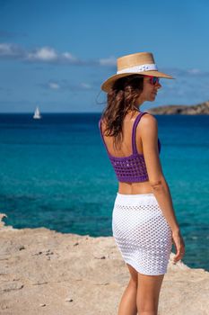 Brunette woman with hat, white skirt and purple top on the shore of the Mediterranean