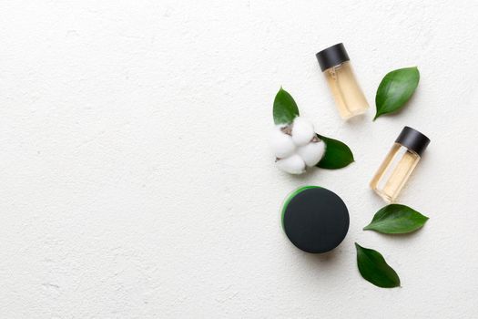 Organic cosmetic products with cotton flower and green leaves on cement background. Copy space, flat lay.