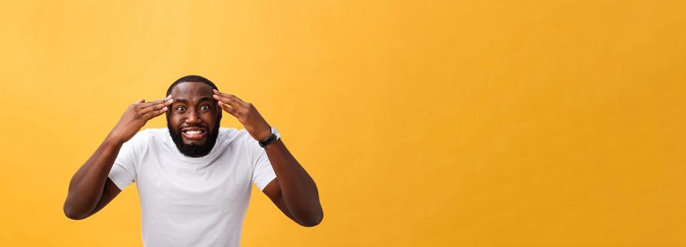 Portrait of african american man with hands raised in shock and disbelief. Isolated over yellow background