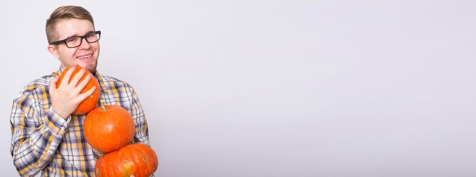 Harvesting, halloween and people concept - Man in black glasses holding three pumpkins over white background.