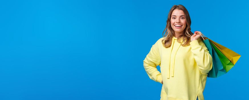 Shopping time. Girl relaxing after hard working days buying things in store on weekend, hold bags on back and smiling relieved, release stress through purchasing clothes, blue background.