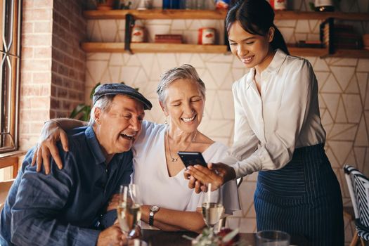 Couple, restaurant and date with a senior man and woman paying their bill with a waitress on her phone. Payment, service and romance with an elderly male and female pensioner on their anniversary.