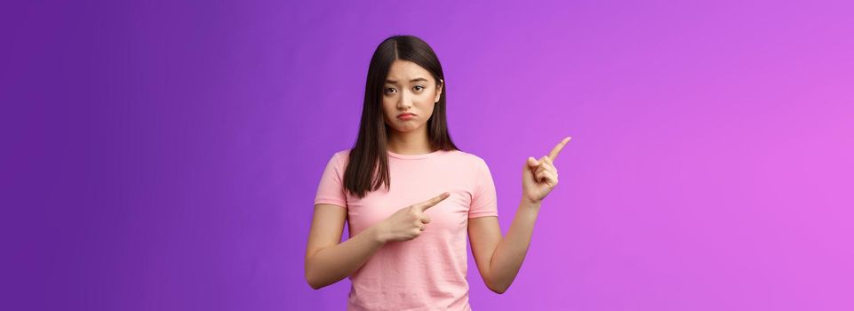 Moody upset whining girlfriend unhappy pointing left, sulking look miserable and distressed, express regret and disappointment, complain bad fortune, stand purple background displeased.