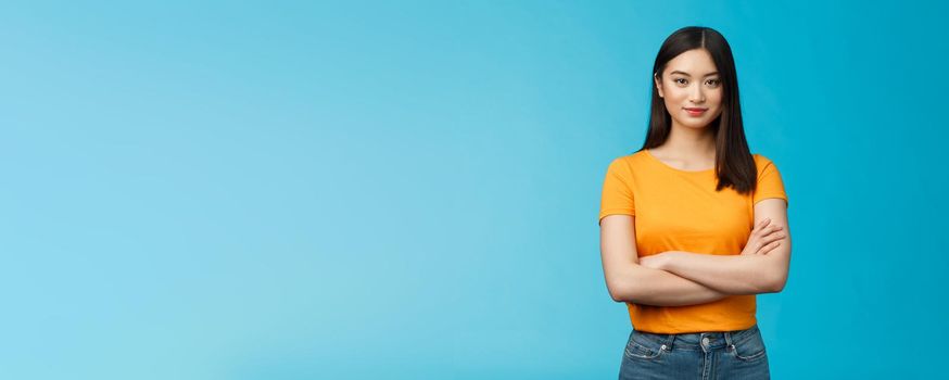 Confident motivated feminine asian woman feel empowered deal office problems manage business, hold hands crossed chest, smiling determined, wear yellow t-shirt, stand blue background.