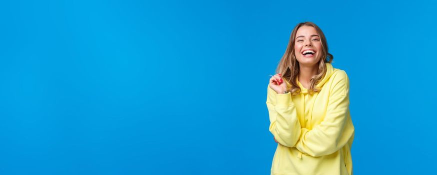 Happy blond young girl laughing from funny joke, having conversation with friends standing near university campus enjoying being in hilarious company, standing blue background.