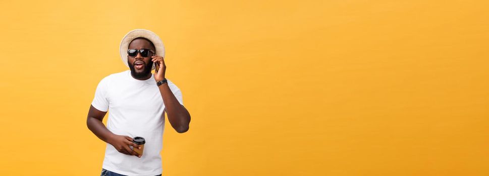 Handsome African American with mobile phone and take away coffee cup. Isolated over yellow gold background