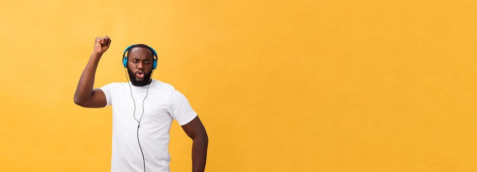 Young African American man wearing headphone and enjoy music dancing over yellow gold Background.
