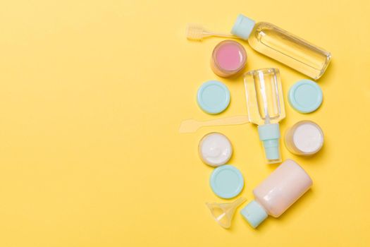 Top view composition of small travelling bottles and jars for cosmetic products on yellow background. Facial skin care concept with copy space for your design.