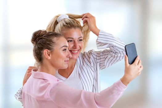 Two girlfriends posing to take a selfie on a clear and blurry background.