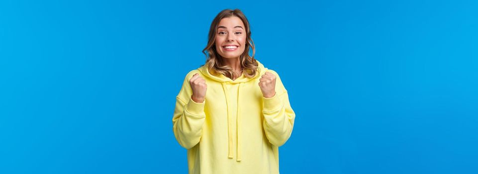 Optimistic and hopeful cute blond girl encourage person do his best, clench fists and cheering with beaming smile, watching game on TV, rooting during match, triumphing over winning prize.