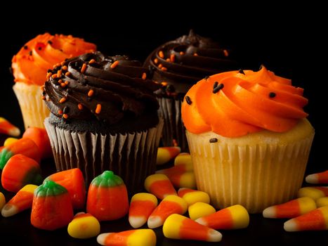 Halloween orange and black cupcakes with candy corn candies on black background.