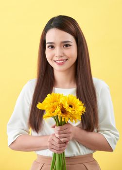 Happy young woman holding bouquet of flowers in her hand on yellow background