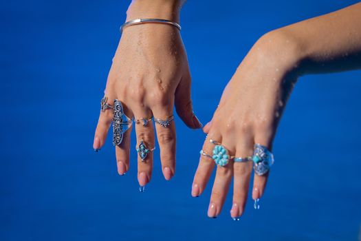 Beautiful gypsy woman demonstrates boho jewelry, rings with turquoise stones on hands. Girl in white dress showing accessories in blue water. Femininity, trend, hippie style concept.High quality photo