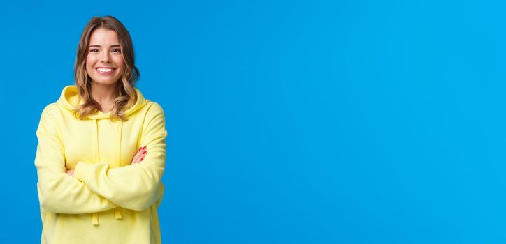 Lets get business. Confident smiling cheerful blond woman with white perfect smile, cross hands chest ready for tasks, listen to boss instructions, standing yellow hoodie over blue background.