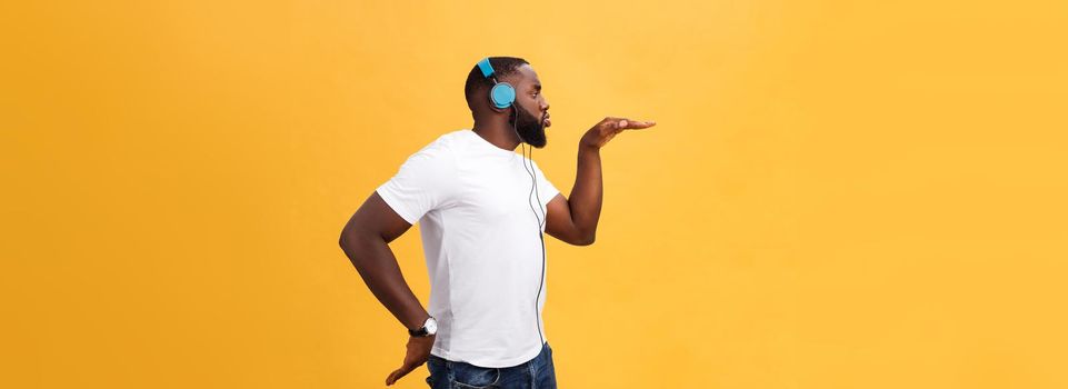 Young African American man wearing headphone and enjoy music dancing over yellow gold Background.