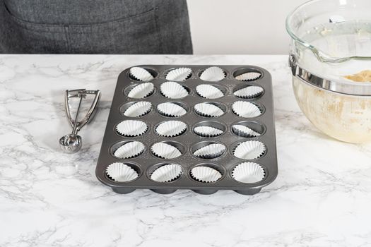 Scooping cupcake batter with dough scoop into a baking pan with liners to bake American flag mini cupcakes.