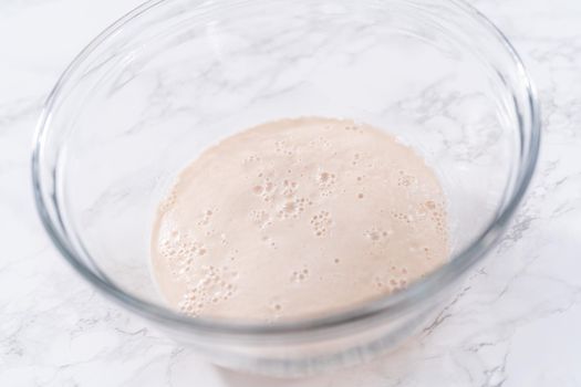 Activating dry yeast in a large glass mixing bowl to prepare the pizza dough.