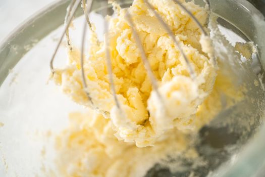Mixing ingredients in a large glass mixing bowl of kitchen mixer to make eggnog buttercream frosting.