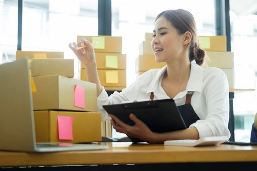 Asian female small online business owner packing boxes on table and checking retail order preparing for shipment. Online business, e-commerce concept.