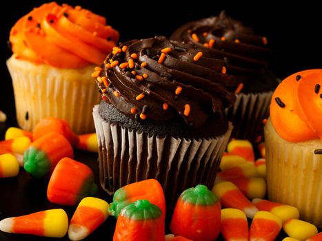 Halloween orange and black cupcakes with candy corn candies on black background.