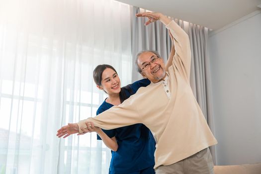 Old senior man enjoys training with physiotherapist for outstretched arms at home, Asian physical therapist patient nursing helping elderly exercising arm stretch, Rehabilitation of disabled concept