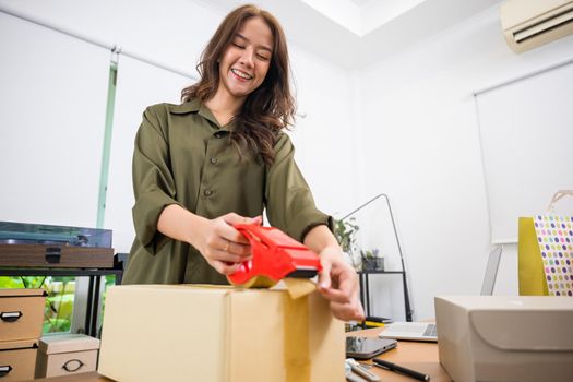 Asian young woman hand packing shipment box with transparency tape at home office, happy freelance and packing cardboard box delivery products to customers, Startup small business, Moving day