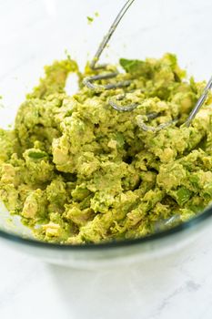 Smashing avocados in a glass mixing bowl to make classic guacamole dip.