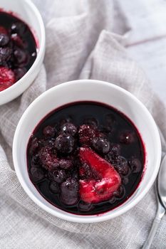 Homemade mix berry compote in small white bowls on a wooden table.
