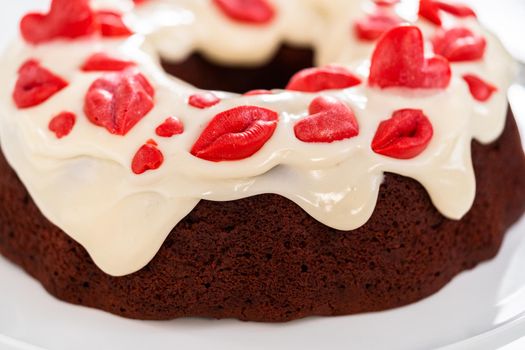 Freshly baked red velvet bundt cake with chocolate lips and hearts over cream cheese glaze for Valentine's Day.