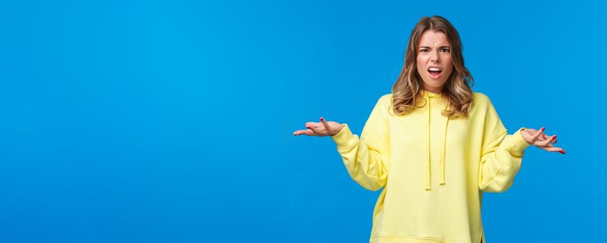 What a heck. Angry and frustrated young woman arguing with person being rude for no reason, shrugging with hands spread sideways in dismay, stare pissed-off and questioned, clueless about problem.