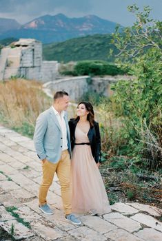 Bride and groom walk hand in hand past the ruins of a stone fortress. High quality photo