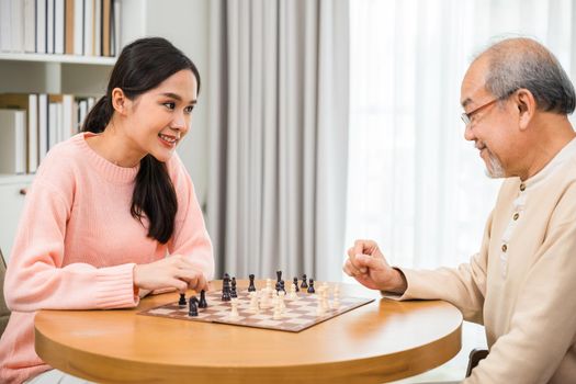 Beautiful young smile woman having fun sitting playing chess game with senior elderly at home, nurse caregiver in nursing home for leisure, Happy active retired people, Healthcare and medical concept