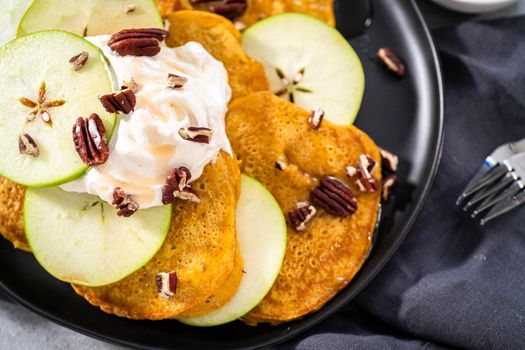 Freshly made pumpkin pancakes with green apples on a black serving plate.