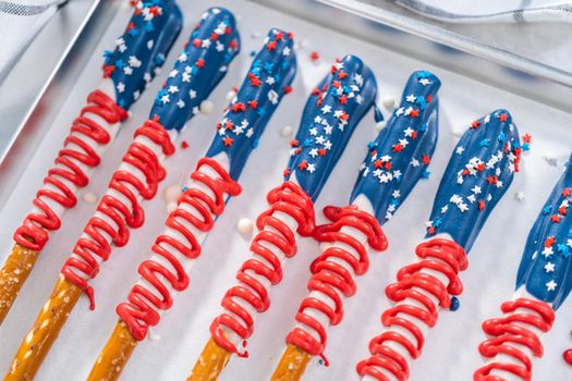 Homemade chocolate-covered pretzel rods decorated like the American flag drying on a baking sheet lined with parchment paper.